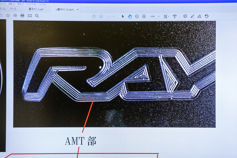 伊藤氏によるA.M.T.の解説。従来はステッカーで表現していたロゴなどをホイール天面にマシニングセンターによる切削加工で入れていく技術だが、写真のように刃物目をあえて残すことで凹凸を連続させる彫刻的な加工とした