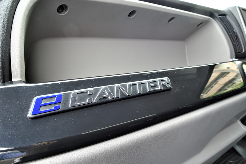 eCanterのキャビン。ディーゼル車をベースにメーター内部の意匠と表示内容をBEV向けに変更。センターディスプレイにはカーナビゲーションやオーディオ情報のほか、車両情報として電池残量、残存走行可能距離、電力消費走行履歴、点検スケジュールなどの表示が可能。Bluetoothによる各種機器との接続もできる。アクセルペダルとブレーキペダルは、ディーゼル車と同じくステアリングシャフト右側に集約されるが、リターンスプリングにはeCanter専用のチューニングが施された