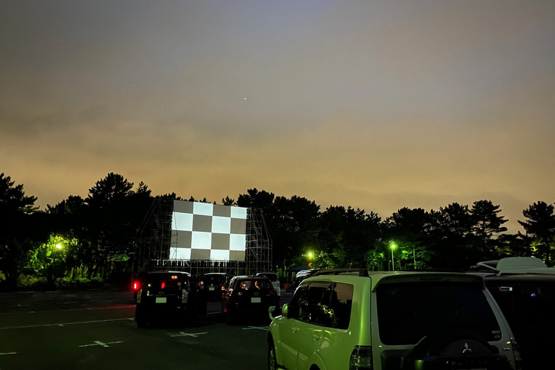 夕闇に浮かび上がるような、ドライブインシアターのスクリーン。8月30日まで稲毛海浜公園駐車場で開催されている「DRIVE IN PARK CHIBA」に参加してきました！　18時過ぎにゴロゴロと近くで雷が鳴り始め、ちょっと肝を冷やしましたが、雨が降ることなく無事に上映されてよかった～。こちらでは、8月28日（金）～30日（日）には、銚子電鉄救済?!“超C級映画”のこけら落とし！　と題して、「電車を止めるな！　～呪いの6.4km～」が上映されるそうですよ