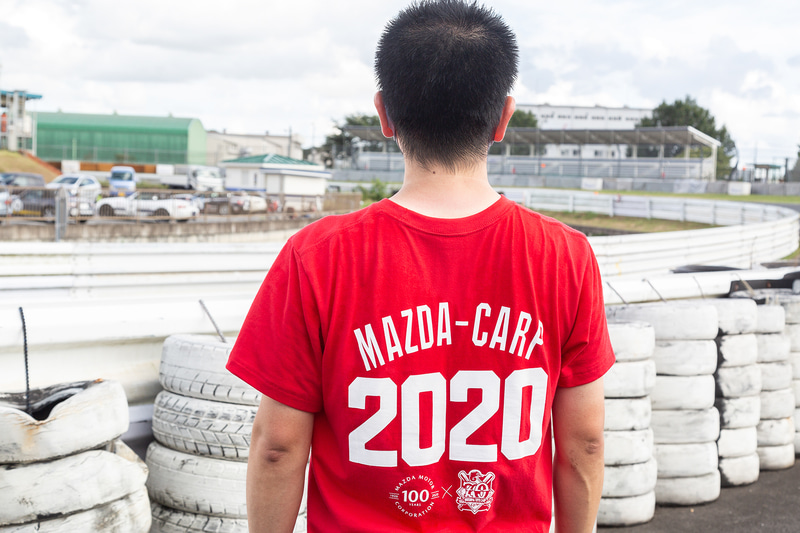 マツダのスタッフはマスクと「マツダ×カープ コラボTシャツ『100TH×70TH』」を着用。マツダ100周年と広島カープ70周年が書かれており、マツダの主なクルマが描かれた上にはその当時のカープのユニフォームが描かれる。カープ坊やの「Be a driver.」ポーズにも注目だ