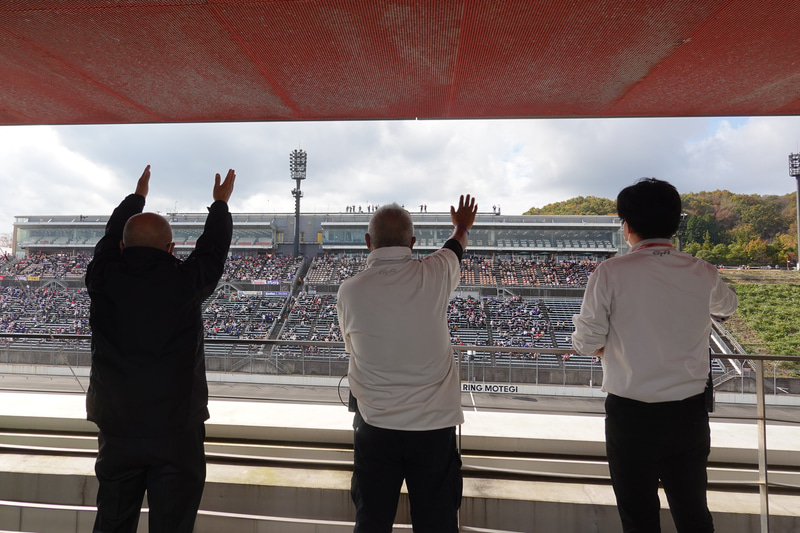 基地局に向かってピットビル屋上からあいさつするGTAスタッフ。左が坂東代表