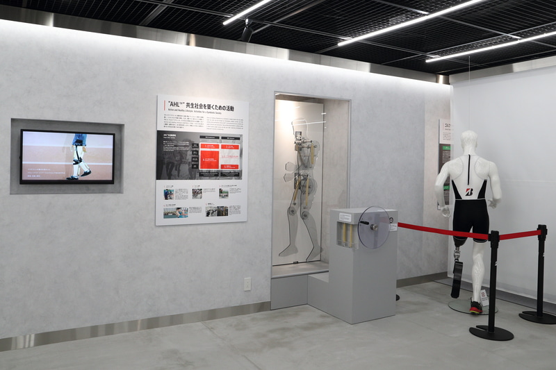 障がい者、ジュニア、シニアをはじめとする全ての人を支える活動「AHL」に関するコーナー。パネルとともにゴム人工筋肉や競技用義足などが展示されている