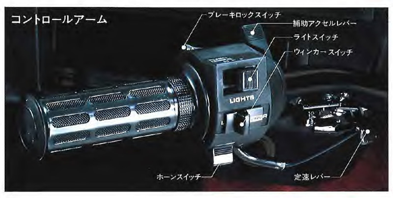 初代テックマチックシステムは、バイクのハンドルのような金属シャフト製のレバーがコラムから伸びたもの。ライトやホーンのスイッチ類もバイクのそれに酷似。操作方法はこのころから今と同様の、レバーを前方に倒すことでブレーキ、グリップを手前に回すことでアクセル