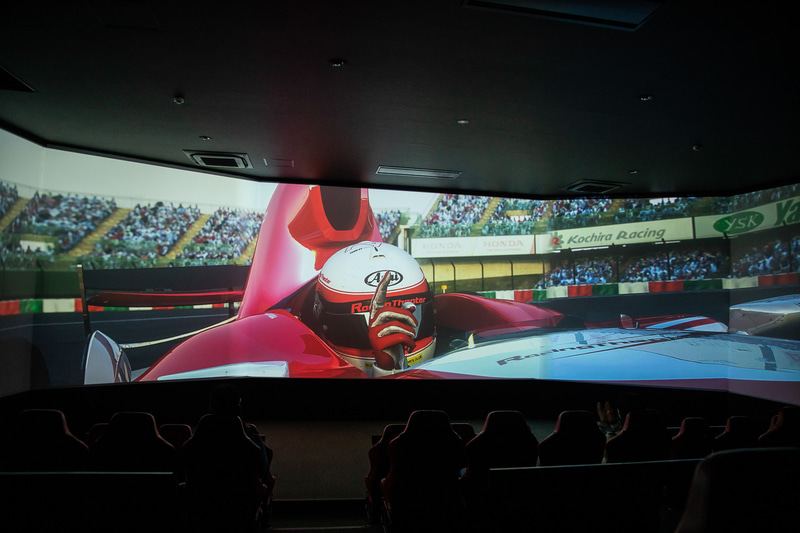 幅19mのワイドスクリーンの前に60席のバケットシートが並び、音と振動でレーシングドライバーが実際に見たり感じたりするスピード感や迫力を体験できる