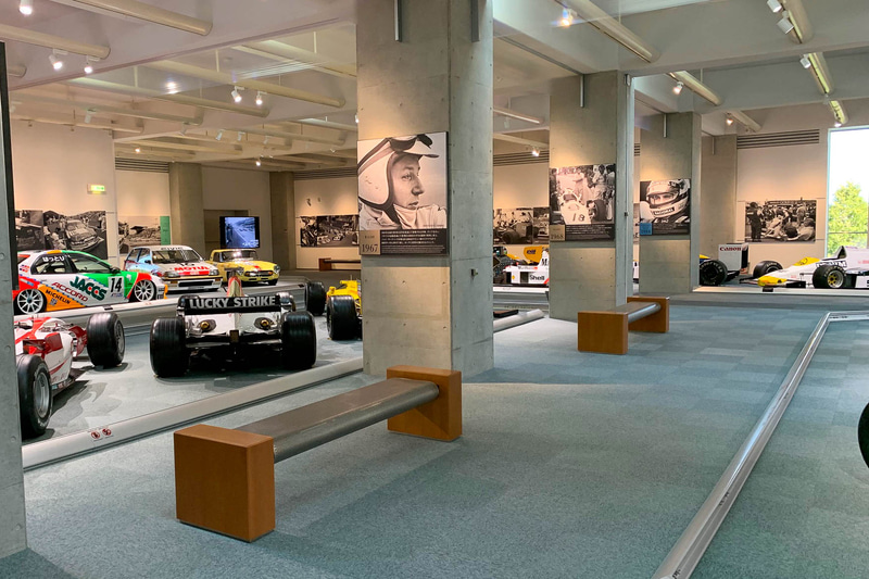 柱にはジョン・サーティーズの写真をはじめ、歴史の一部を切り取った粋な演出が。その向こうには服部尚樹選手のハコの格闘技、JTCCでのシビック、そしてGr.A時代のワンダーシビックやRSCのホンダS800が置かれている