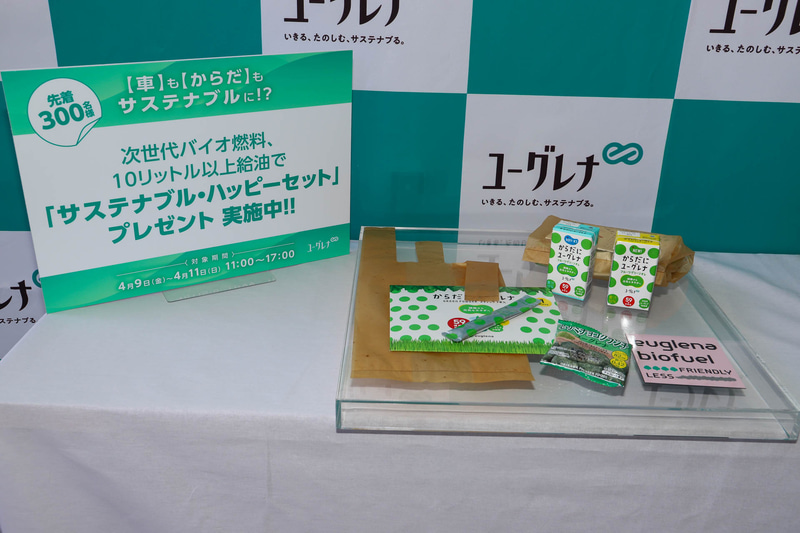 4月9日～11日の3日間、11時～17時に次世代バイオ燃料を10L以上給油した人先着300名に、ユーグレナバイオ燃料の残渣を利用したバイオプラスチック袋や、食用ミドリムシを使用した「からだにユーグレナ」「セサミチョコクランチ」といったユーグレナ製品をセットにした「サステナブル・ハッピーセット」がプレゼントされる
