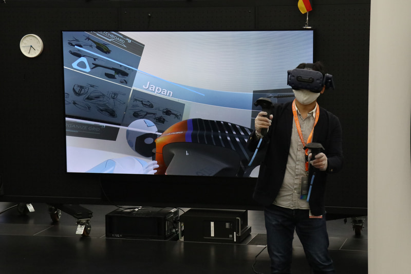 ゴーグルを付けてVR空間にいるデザイナー。後方のモニターはゴーグルを付けていないほかのスタッフのためにある