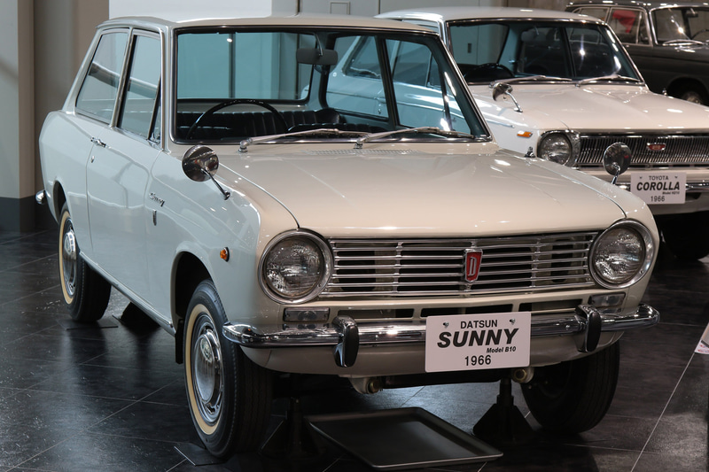 1966年発売、日産・サニー（B10型）。988cc水冷4気筒OHVエンジン搭載。セドリック、ブルーバードの下位、エントリーモデルとして製品化、カローラとは長年のライバルとなった。サニーもカローラ同様、発売時は2ドアセダン（トヨタ博物館展示車）