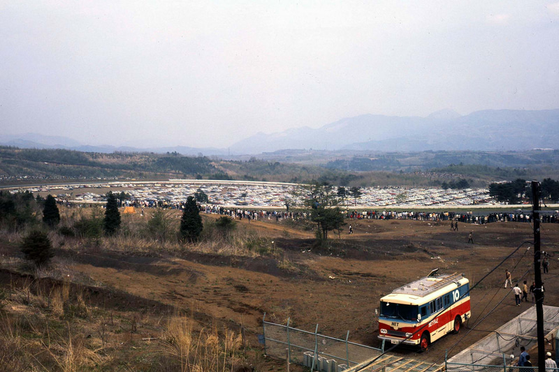 1970年JAFグランプリ。現在のコカ・コーラコーナー付近の風景。S字と250Rに挟まれる駐車場、コース沿いの人並みが見られる。手前のNETテレビ、10と書かれた中継車は日本教育テレビ、現在のテレビ朝日の車両