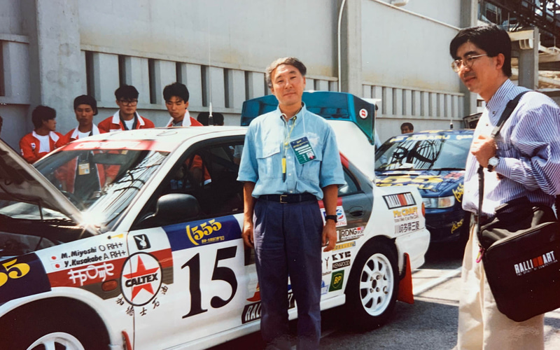 車検場で記念写真。まだラリー前なので私服です。右で書類入れのバッグを持っているのは、サービスもやってくれたナビゲーターの石垣勤くん。後ろの555カラーはスバルチームです