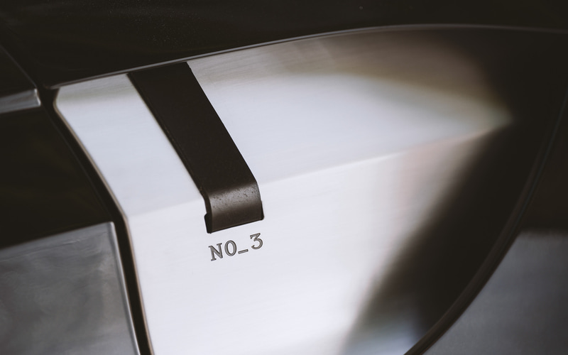 サドルレザーストラップを備えたユニークなサイドフェンダーパネルは、1921年に製作されたA3の露出したアルミニウムボンネットと、それを固定したボンネットストラップからヒントを得たという。さらに、オリジナルモデルに刻印されていた「No-3」の文字も再現している。右はA3に刻印されている「No-3」の文字