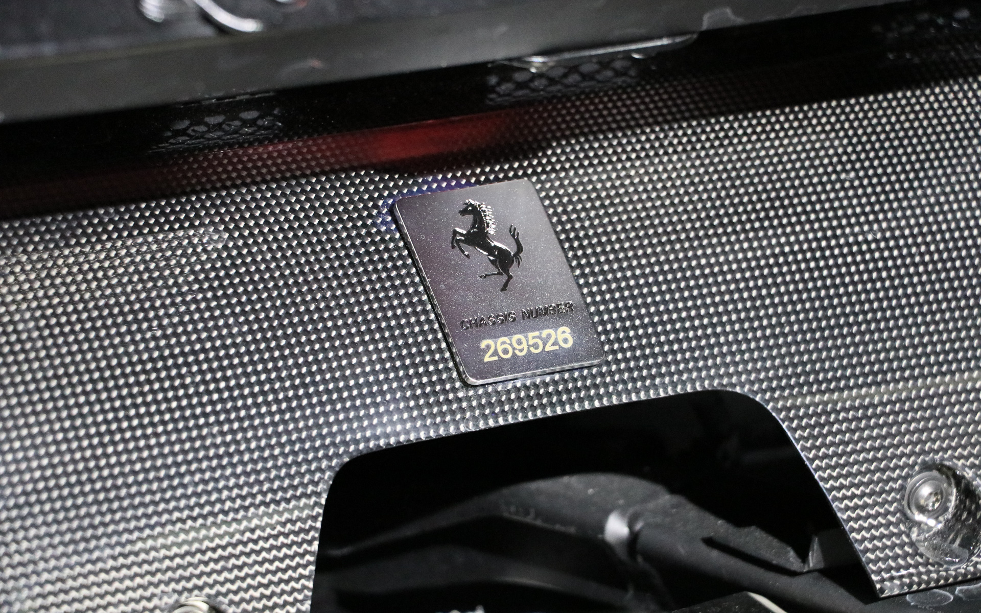 エンジンルームのカーボンカバーにはシャシーナンバーが記されたプレートが貼られている