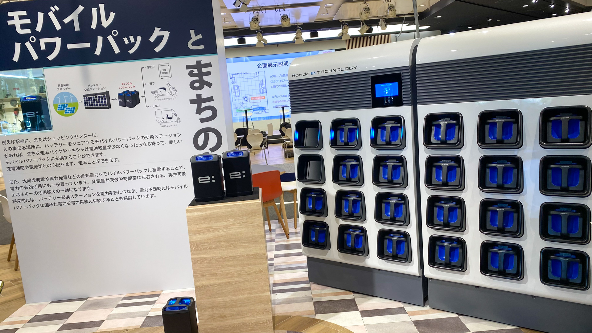 モバイルパワーパックe：は、縦30cmほど、横18cmほど、奥行き16cmほどのリチウムイオン電池で、50.26V、26.1Ah/1314Wh。重さは10.3kgで価格は1個、8万8000円となっています。交換ステーションはこんな感じで、24個の充電口がある小さなコインロッカーみたいな印象。カードをかざすと、最初にカラになったバッテリを入れる場所が光り、入れ終わると今度は満充電になっているバッテリが光り、それを抜いて自分のモビリティに搭載するという仕組みです