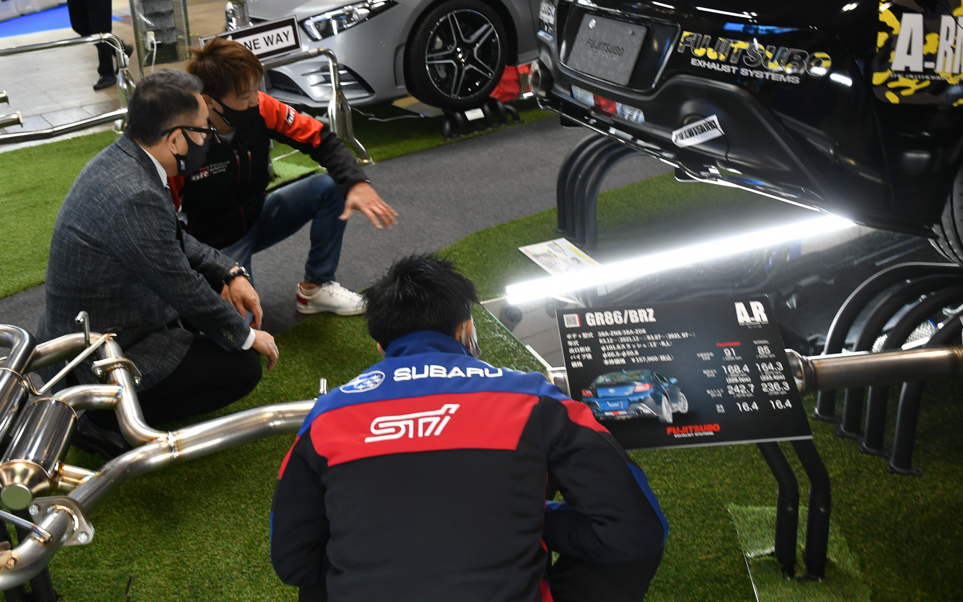 フジツボのブースで佐々木雅弘選手（奥）、井口卓人選手（手前）と一緒にマフラーをのぞき込むモリゾウ選手ことトヨタ自動車 代表取締役社長 豊田章男氏（中央）