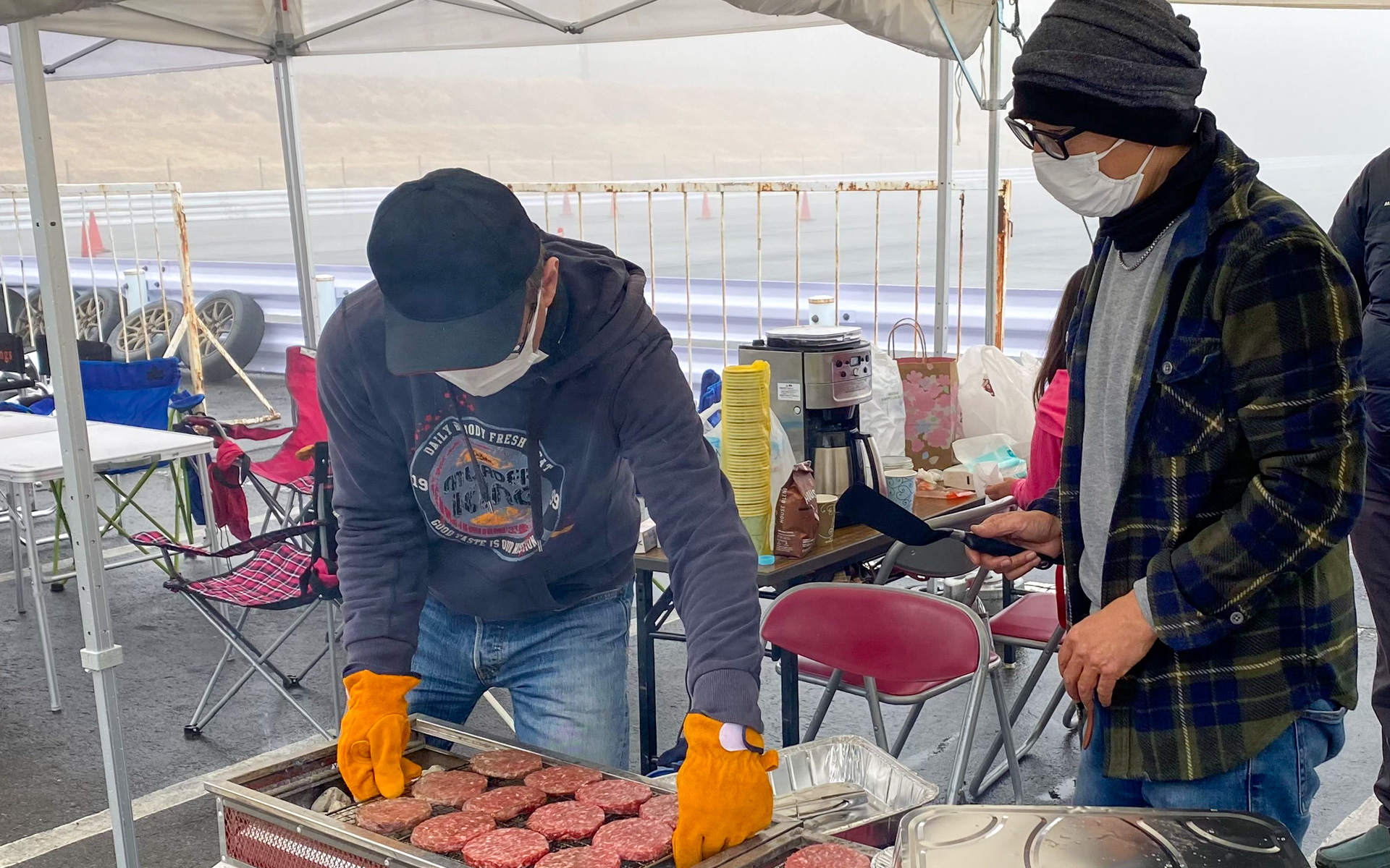 自身もクルマ大好きDJでドリフトも上手なピストン西沢アニキ（右）が、クルマ好き仲間のために自腹で買い出しから準備、調理までやってくれる豪華BBQ。この日のメインはお肉がバンズからはみ出しそうなBIGバーガーでした。最初に炭で肉を焼き、その後スモークチップでじっくり肉をスモークするという“ひと手間”が、さすがBBQの達人ですよね