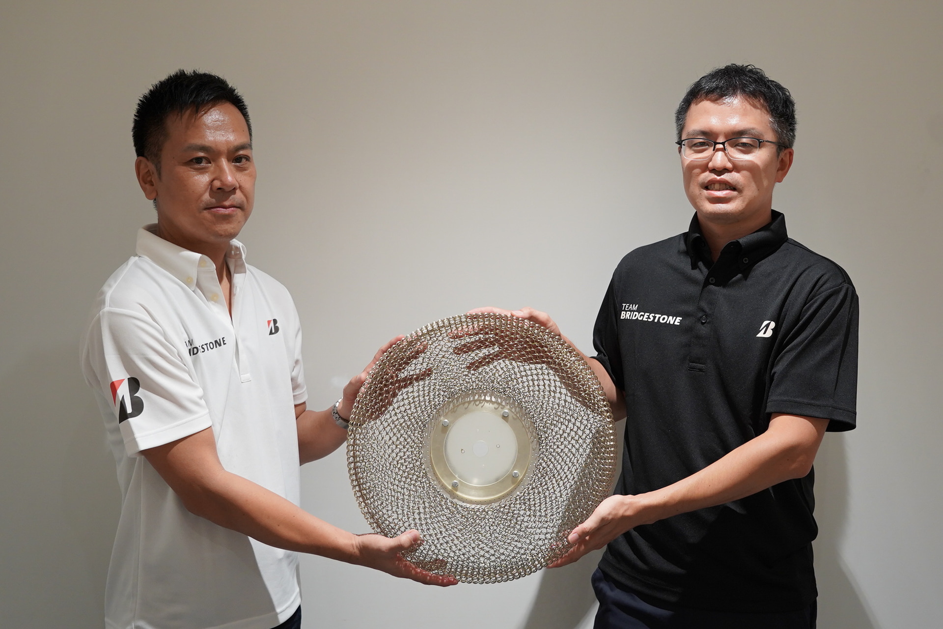 月面探査車用金属タイヤの模型を持つ、株式会社ブリヂストン 次世代技術開発第2部 弾性接地体開発課長 片山昌宏氏（左）と同 弾性接地体開発課 今誓志氏（右）