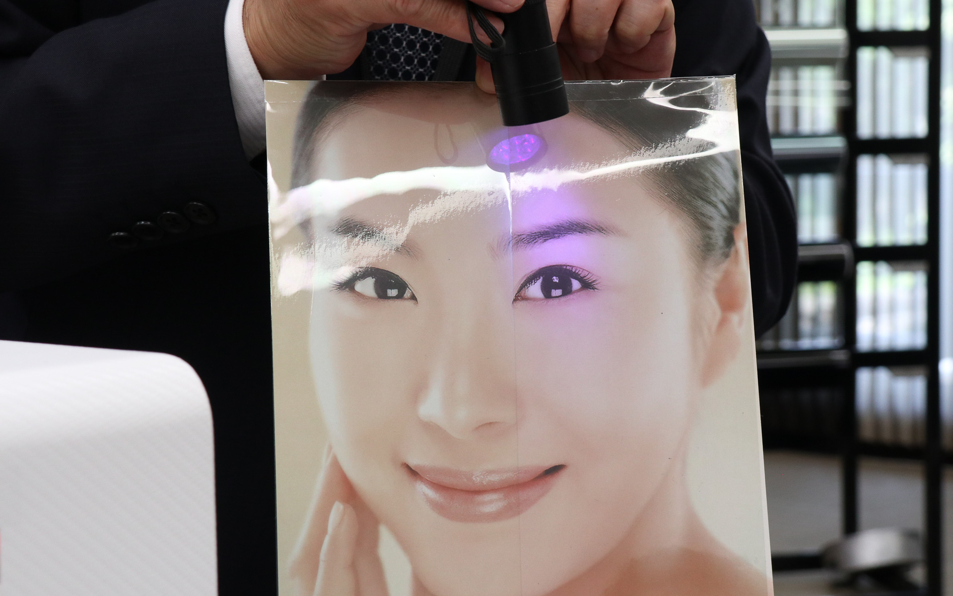 ブラックライトのUV光を当てると左側の他社製品は白っぽい反射で写真が見えにくくなるが、ahead製品を貼った右側は写真がクリアなままとなっている