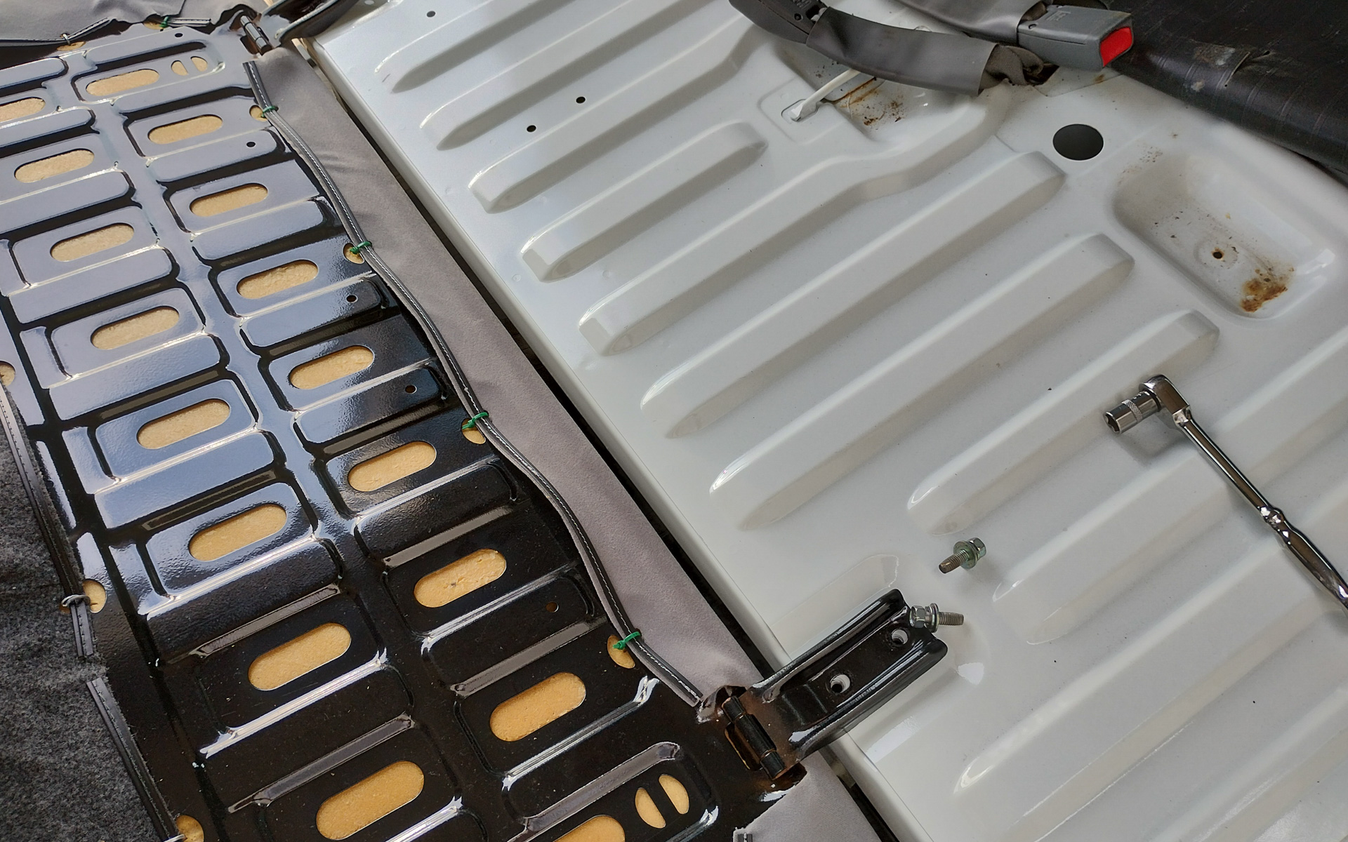 リアシート下にアクセスするためにはシートを外し、この白いパネルを外すと便利だが、外すためには下回りからアクセスし、マフラーの遮熱板まで外す必要があるため通常は外せないと思ったほうがいい