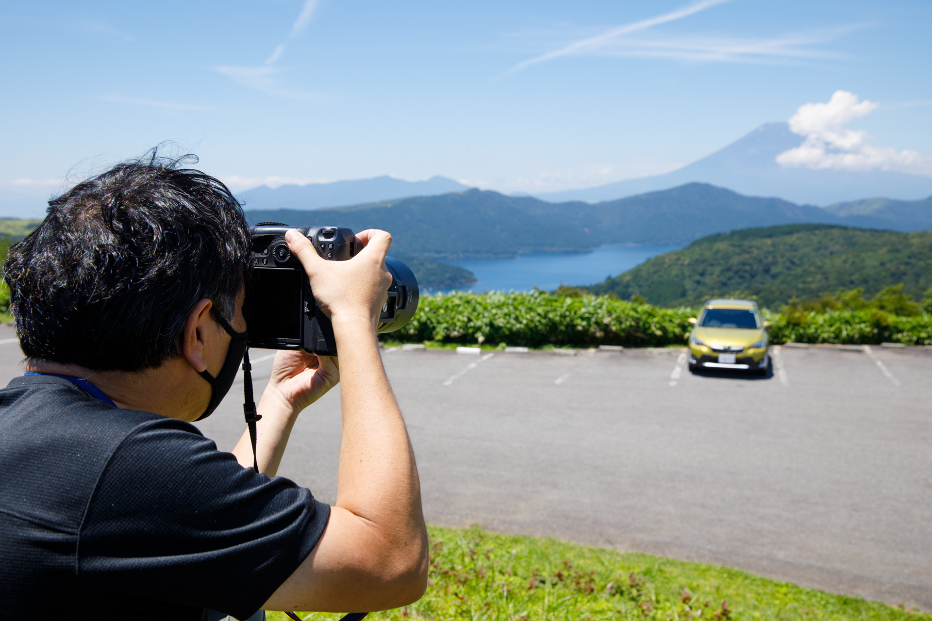 「ゆるCar写真」の撮影風景。広く風景を写したいのでレンズは広角から標準あたりが使いやすい。なお、この写真に写っているように、白線や車止めがあって、そのままでは「うるさい」写真になってしまう。不要なものは消して落ち着きのある写真にしよう