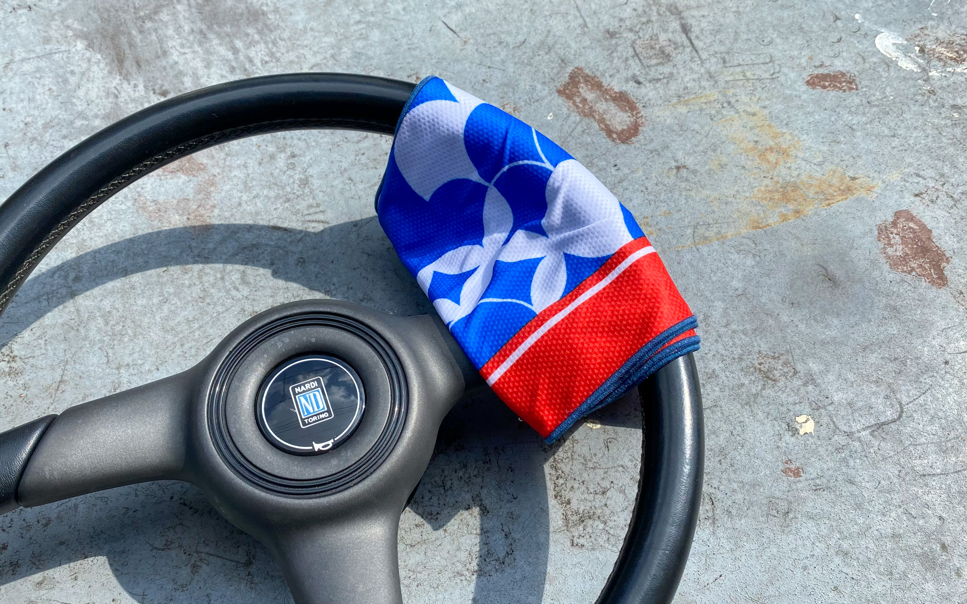 この夏もいろんな冷感グッズが売れていたようですが、これは水で濡らして絞るだけで、ヒヤッと冷たくなるという冷感タオル。今や100円ショップでも手に入ります。炎天下での駐車時に、熱くなったハンドルやシフトノブ、チャイルドシートの金具などにうっかり触ると火傷する危険性もありますが、そんな時は冷感タオルをのせて数分冷やすと、安心して触れるようになるのでぜひお試しを（写真は、使い方がわかりやすいようにベランダで再現してみたものです）