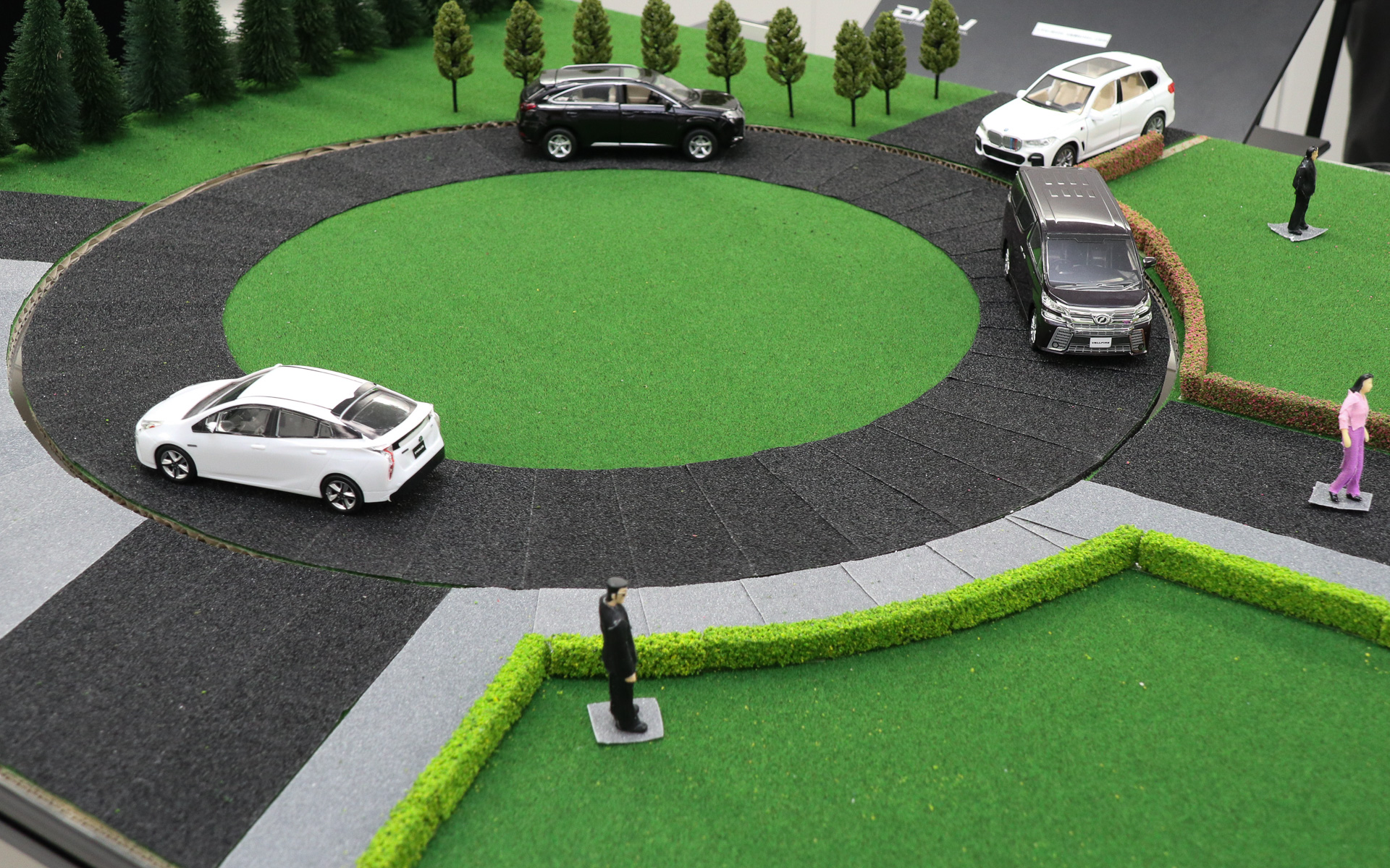 デモ機の前方に歩行者を模したフィギュアやミニチュアカーなどを配置。中央のターンテーブルが回転して車両の走行を再現し、RGB-IRセンサの画角に手前の黒い服を着た男性から画面奥の白いSUVまですべて収まるようレイアウト