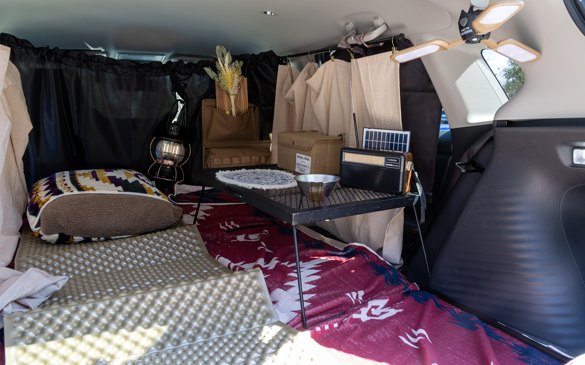 ペットボトルや軽食などが置けるようメッシュテーブルを積む。スマホやクルマのリモコンキーをしまっておく小物入れもあると便利だ。また、ラジオなど気に入っている小物を持ち込むのもいい。知らない町で車中泊をしながらローカルのラジオ放送を聞くのも楽しそうだ