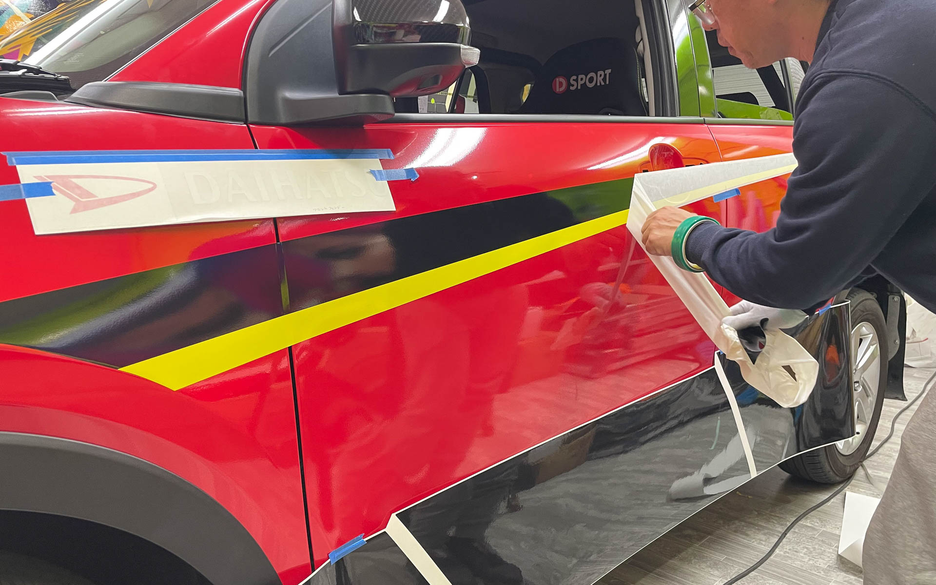 カービューティープロの手によってラリチャレ仕様のラッピングが施されるロッキー。特徴的なコンパーノレッドのボディカラーにラッピングがされたように見えるが、実はブラックのボディカラーの車両をフルラッピングしたという手が込んだ仕様