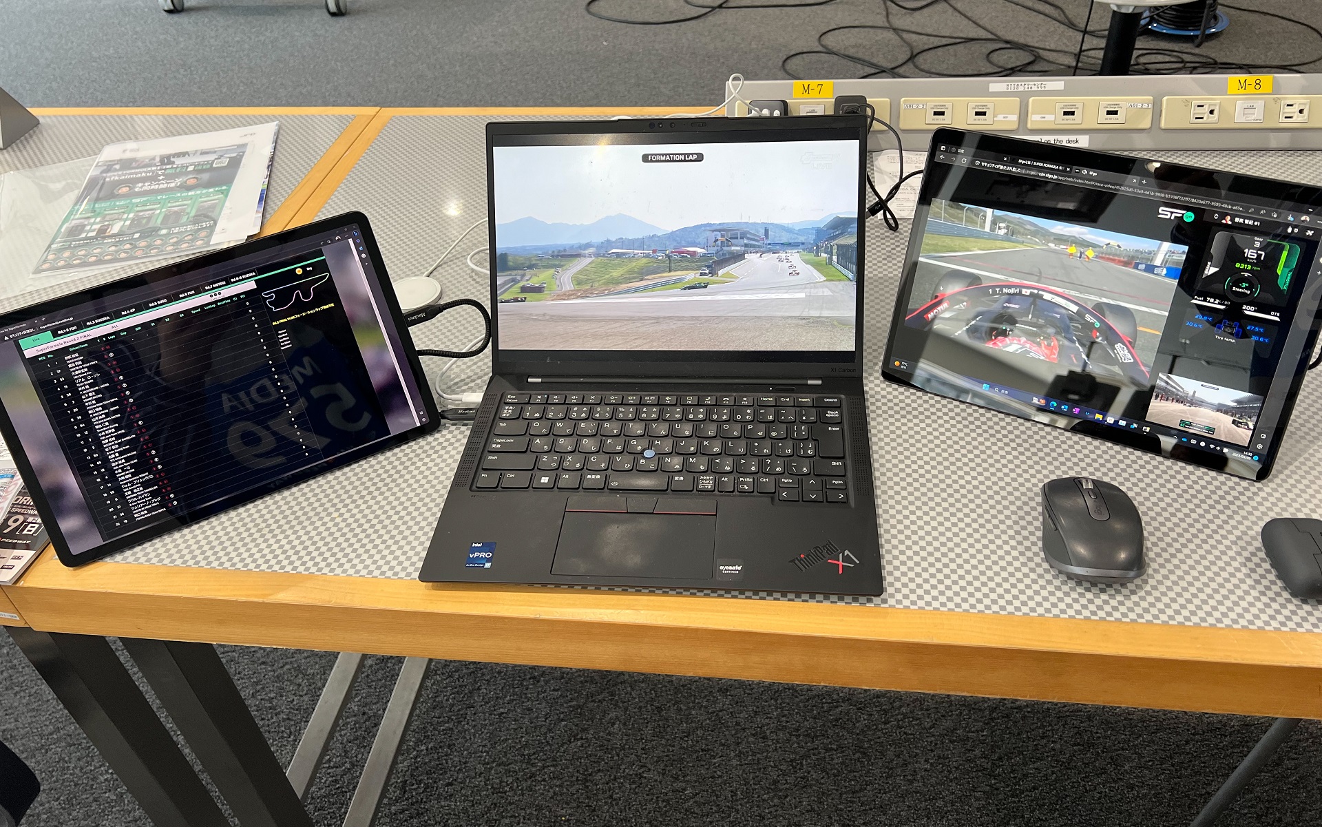 筆者の視聴環境。左右タブレットの左側にライブタイミング、右側にSFgoを表示させている。そして中央のPCでは中継（JｰSPORTS）を自宅にあるBS放送を受信して遠隔地から視聴できるHDDレコーダーにVPNで接続して視聴した。なお撮影しているiPhoneでも手元用にSFgoを表示している。中央のテレビ中継の画面ではすでにフォーメーションラップがスタートしてポールの野尻選手が1コーナーにいるが、左側のSFgoではまだ動き出していないことがこの画面でも分かる。このようにSFgoでは若干の遅延がある。