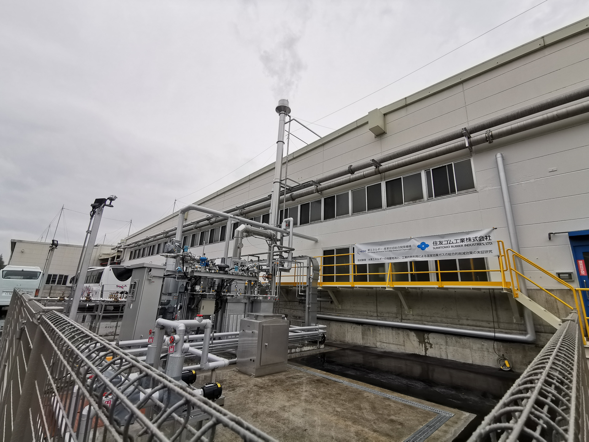 高精度メタルコア製造システム「NEO-T01」の加硫工程のある建屋の外に水素ボイラーが設置されている。煙突からは水蒸気が出ている