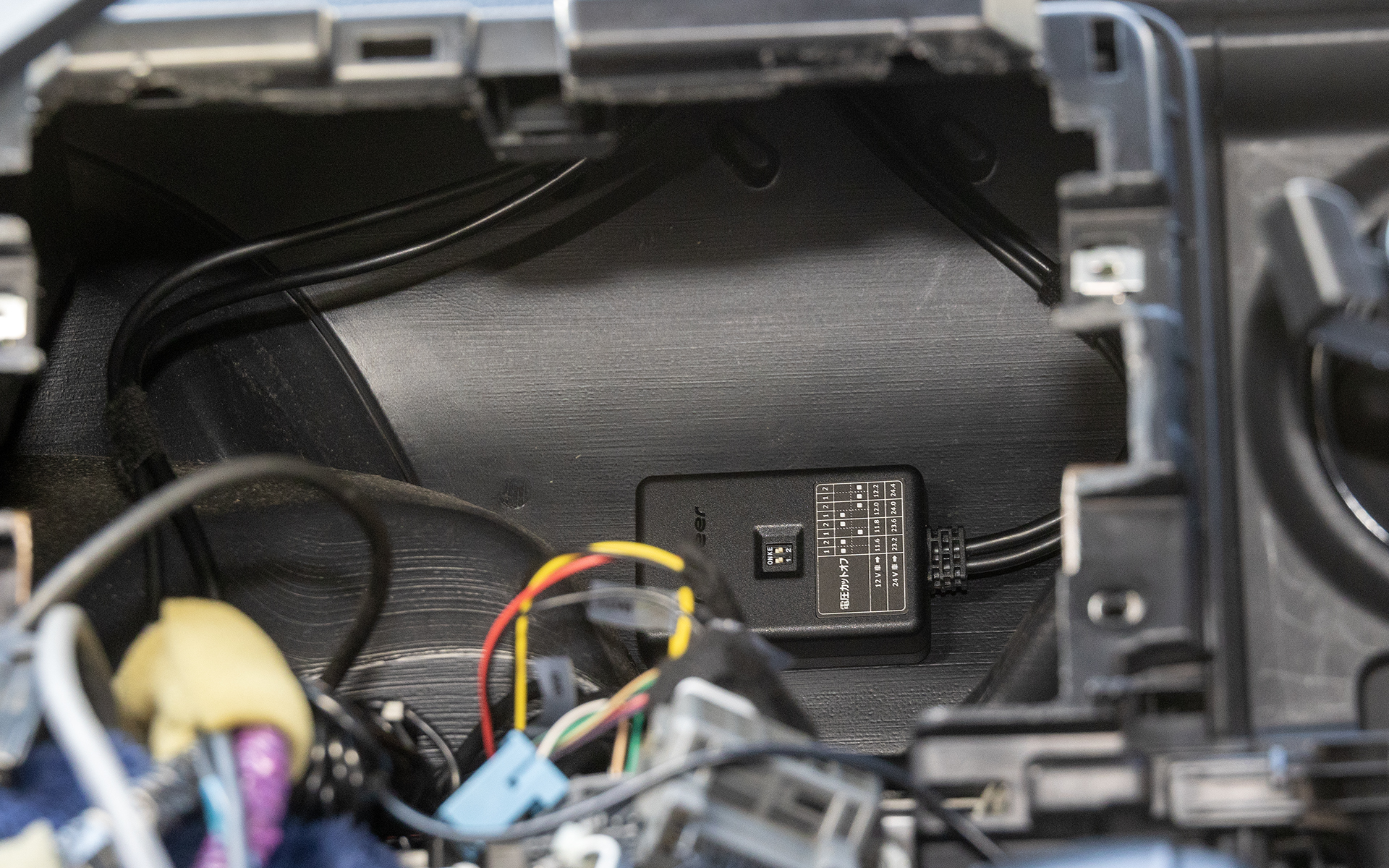 本体はバルクヘッド側に両面テープで固定。工場出荷時の電圧カット設定は11.6V（12V車）だが、バッテリが弱っているクルマだとバッテリ上がりを起こすかもしれないとのアドバイスから、12.2Vを下まわると常時電源の供給を止める設定とした