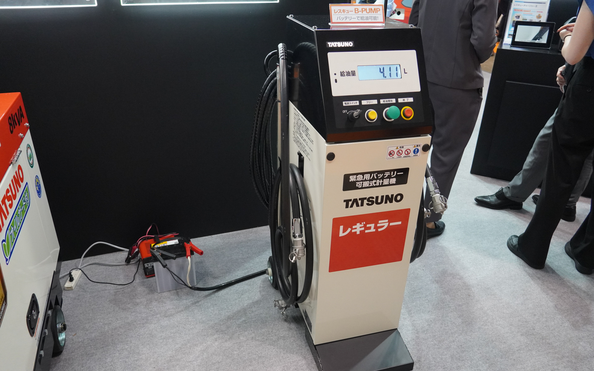 タツノは停電時にも使える12Vバッテリーで動く可搬式計量機を展示。実際に2019年の千葉県の大規模停電の際に、停電で動かないガソリンスタンドで使い、ガソリン供給を行なった。左側に置いてある車載バッテリで実際に動作させている