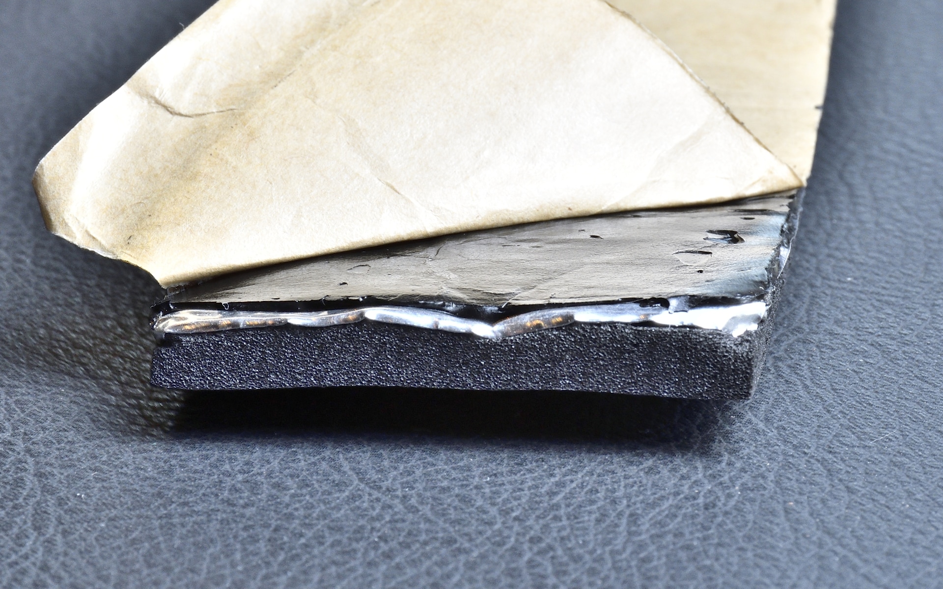 2kHz以上の比較的高い周波数帯域を含む、より幅広い音域の走行騒音をバランスよく吸収するようにチューニングしたニトリルゴム発泡体による「半連続気泡構造吸音層」をベースに、従来比約2倍の厚さのアルミシートを投入して高い遮音性を実現する「肉厚アルミ遮音層」と、施工対象面への強固な追従性により不要振動を抑え込むブチルゴム製の「超強粘着制振層」を一体化させた独自の3層構造となっている