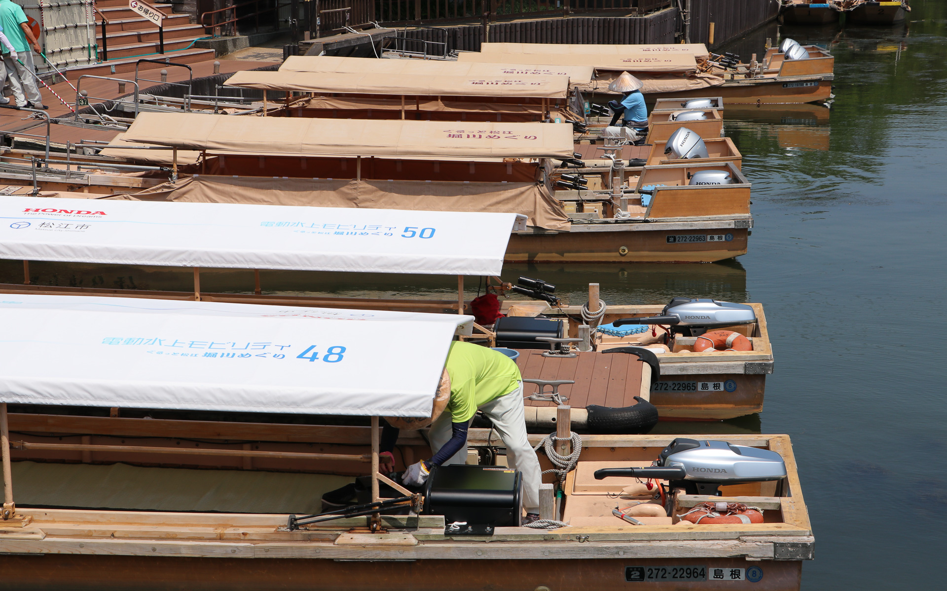 奥に停船しているのが従来のエンジン船外機搭載船、手前の白い屋根の遊覧船が実証実験に使う電動推進機プロトタイプ搭載船