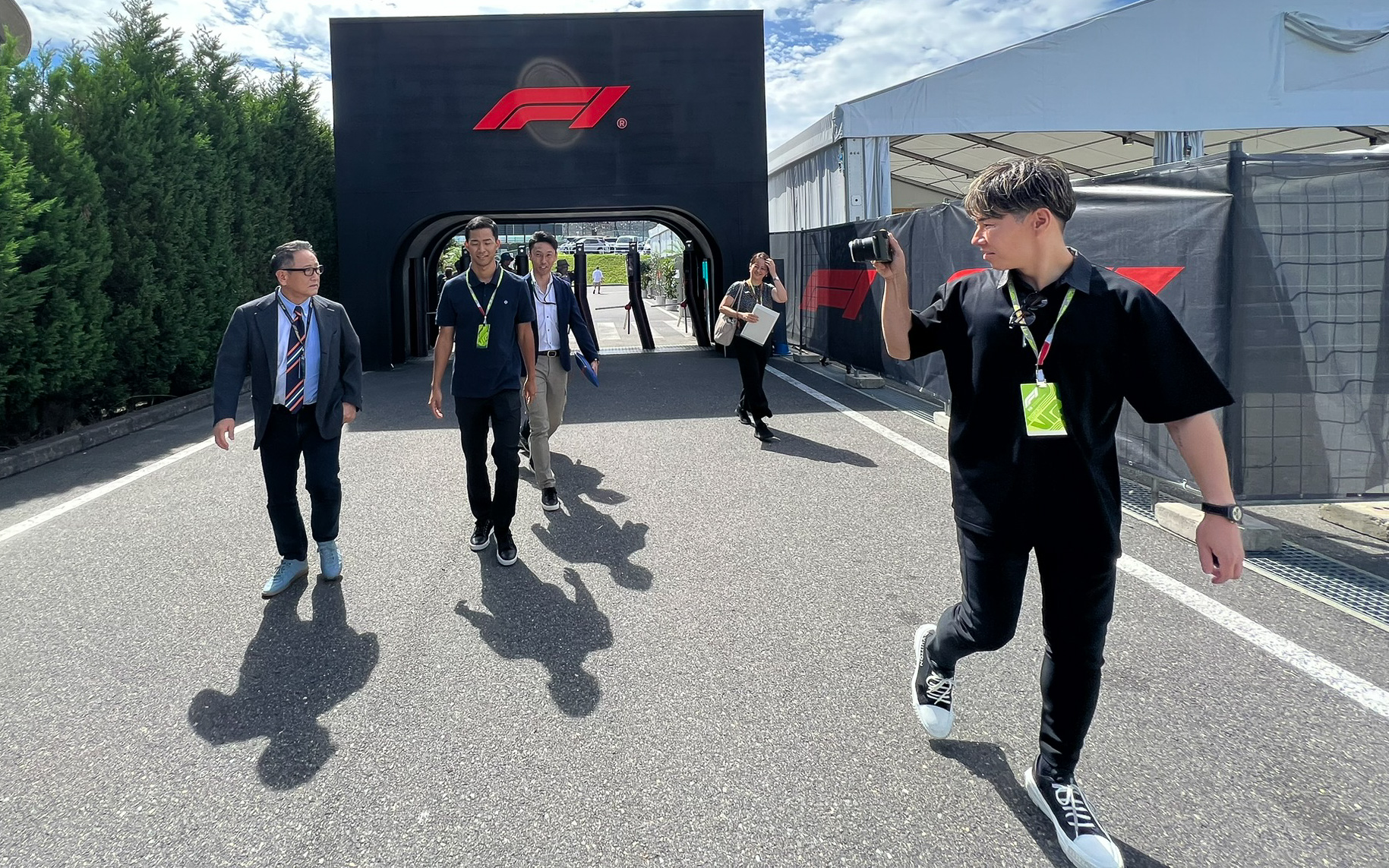 F1が描かれたパドックゲートをくぐる豊田章男会長。なぜか小林可夢偉選手（右）はカメラマン。この写真に元F1ドライバー2人と、ル・マンウィナー3人と、未来のF1ドライバーが写っている。あ、ニュルブルクリンク24時間ドライバーも