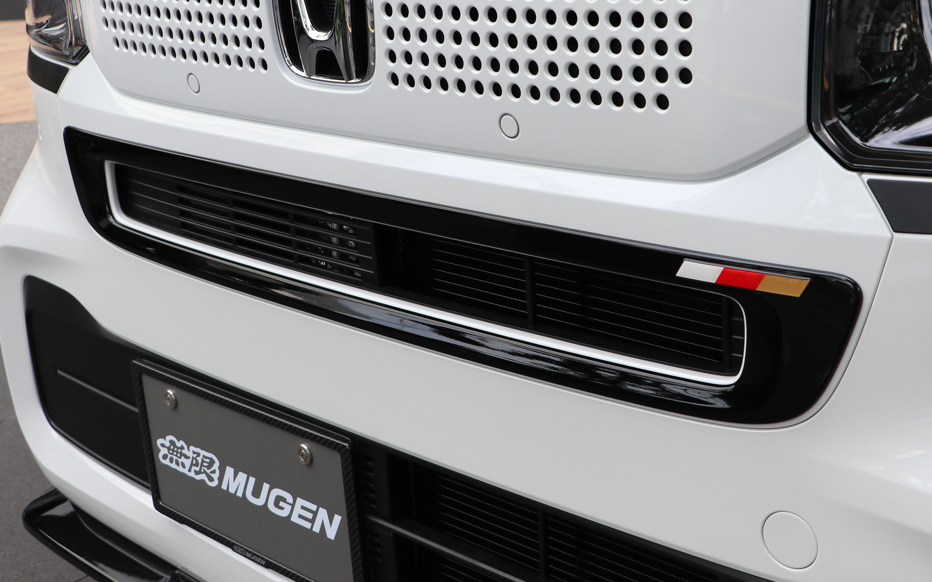 純正グリルにかぶせて装着する「フロントグリルガーニッシュfor N-BOX」の価格は、カラード2色（プラチナホワイト・パール、クリスタルブラック・パール）が3万5200円、未塗装2万4200円