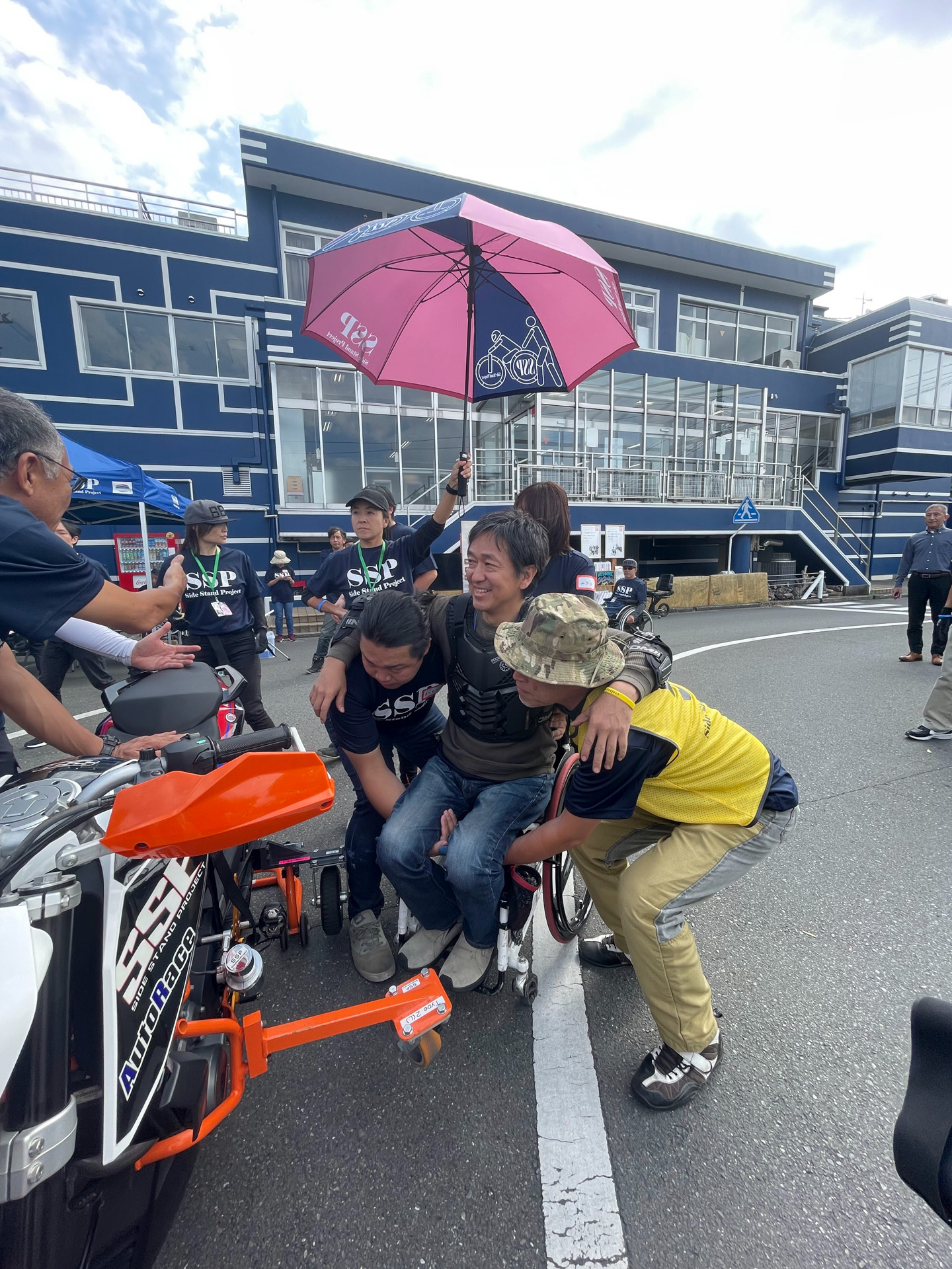 スタッフさんに抱え上げられて車いすからバイクに移動。足もビンディングにセットしてもらう