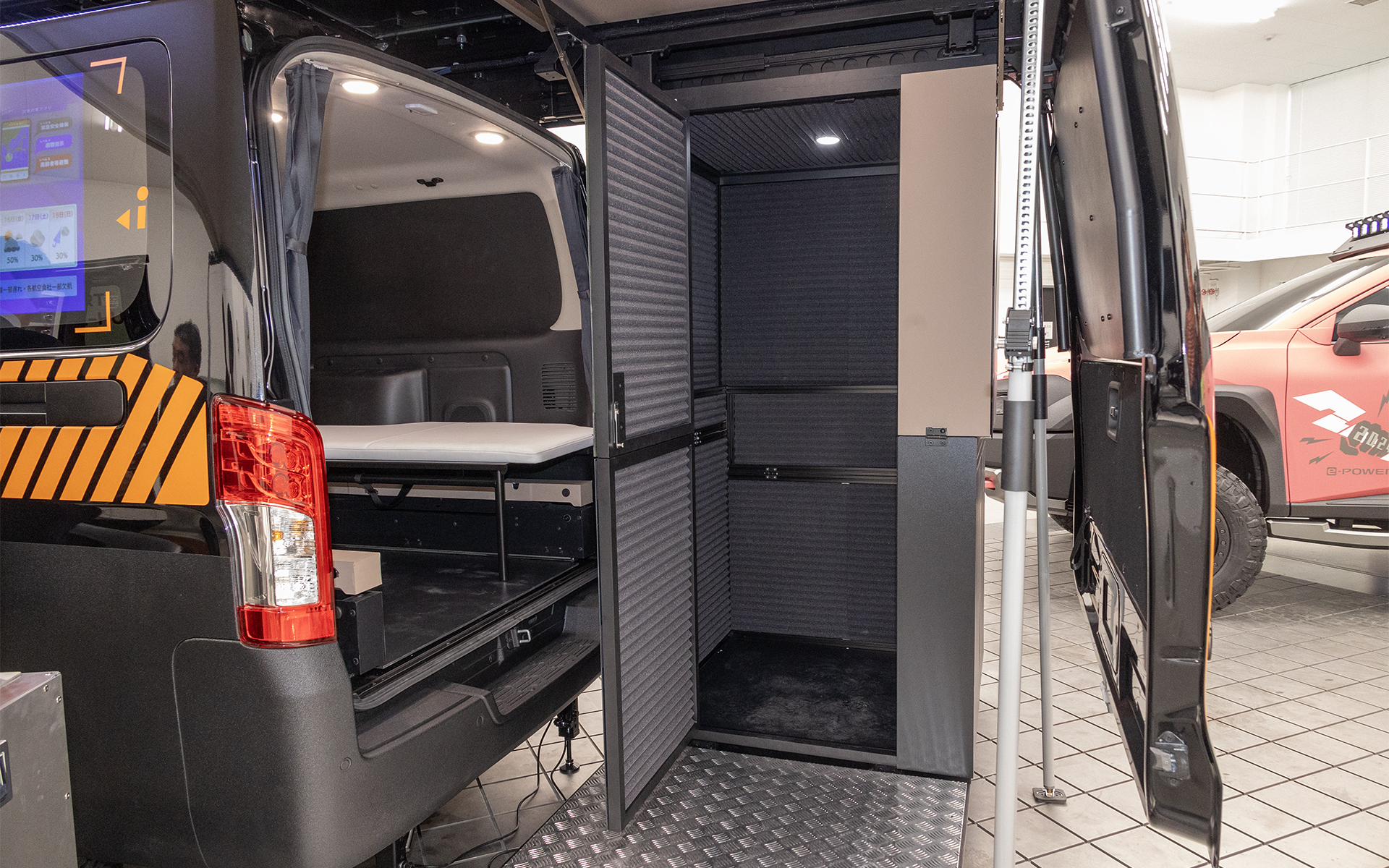 テールゲートは上に開くのではなく、ルーフに追加されたレールで後方にスライドする。そして作ったスペースにはプライバシーが守られる防音個室を設けた。素材には軽量遮音材（音響メタマテリアル）を使用