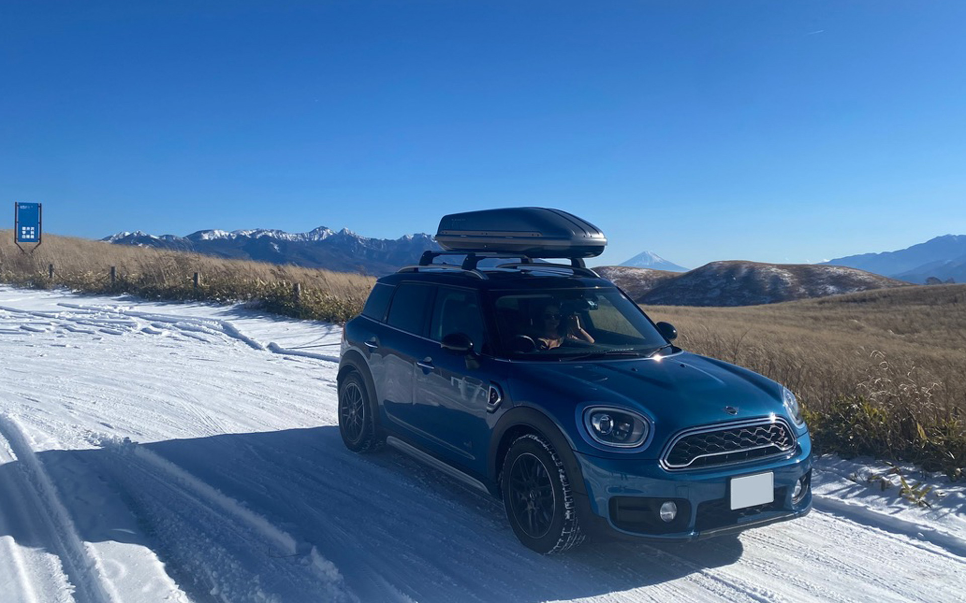 MINI純正のルーフボックスを搭載した愛車と雪景色をパチリ。遠くに富士山も望めました。「キャリアをもっとルーフにペタペタに低くした方がかっこいい」と言う、ルーフボックス使用歴の長い先輩からのアドバイスがあったようですが、ガラスルーフが開けられなくなったら困るので、最初はこのくらいにしておきました（笑）