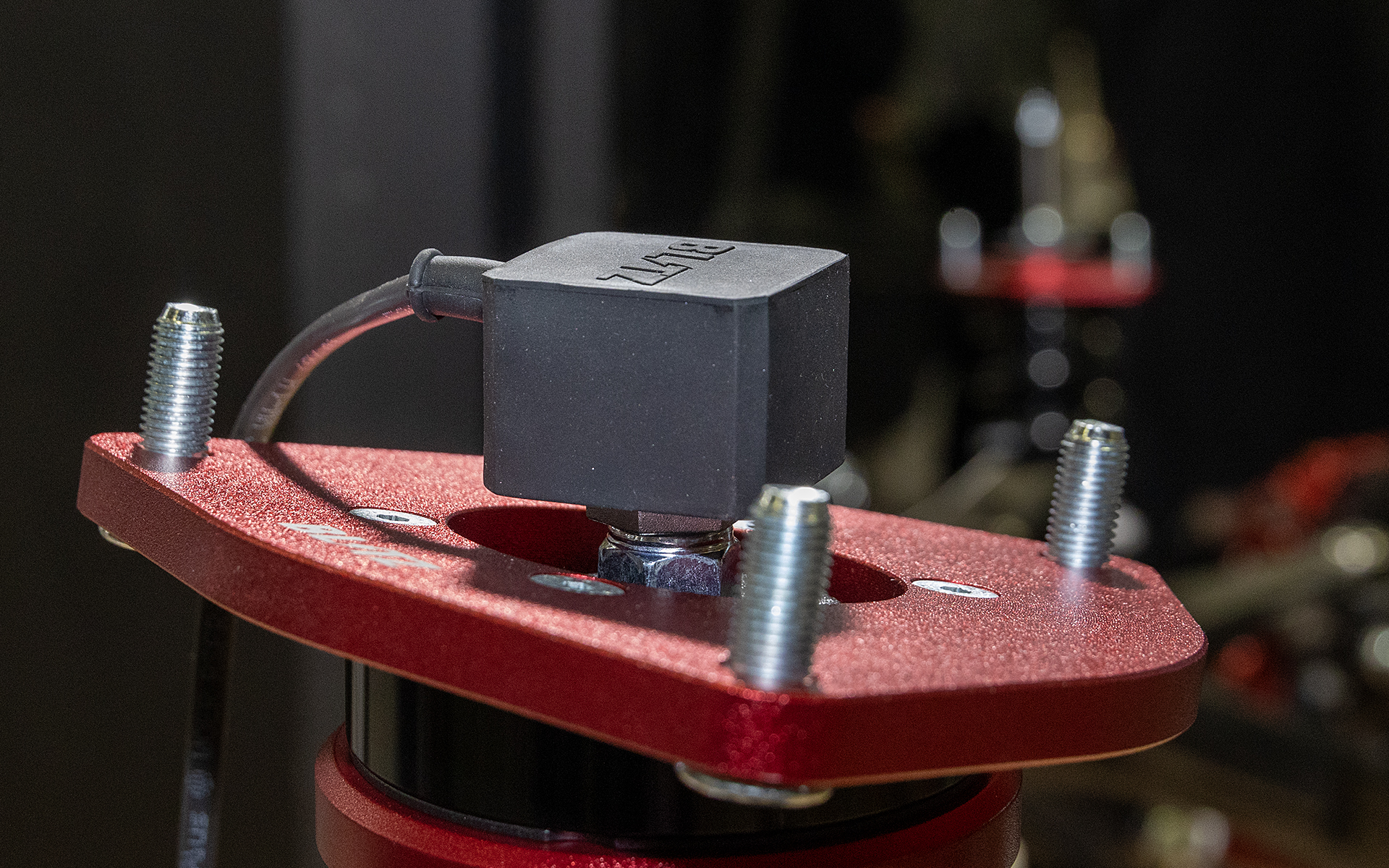 サスペンションにある減衰力調整ダイヤルをモーターで回す機構.。室内に付けるコントローラーの操作により減衰力を任意で調整できるほか、コントローラー内蔵のGセンサーからの信号により走行シーンにあった減衰力のフルオート制御も可能