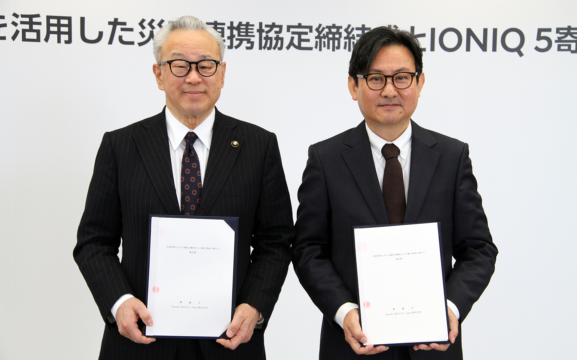 協定書をもって記念撮影に応じる浅井由崇市長（左）、Hyundai Mobility Japan 代表取締役社長の趙源祥（チョ・ウォンサン）氏（右）