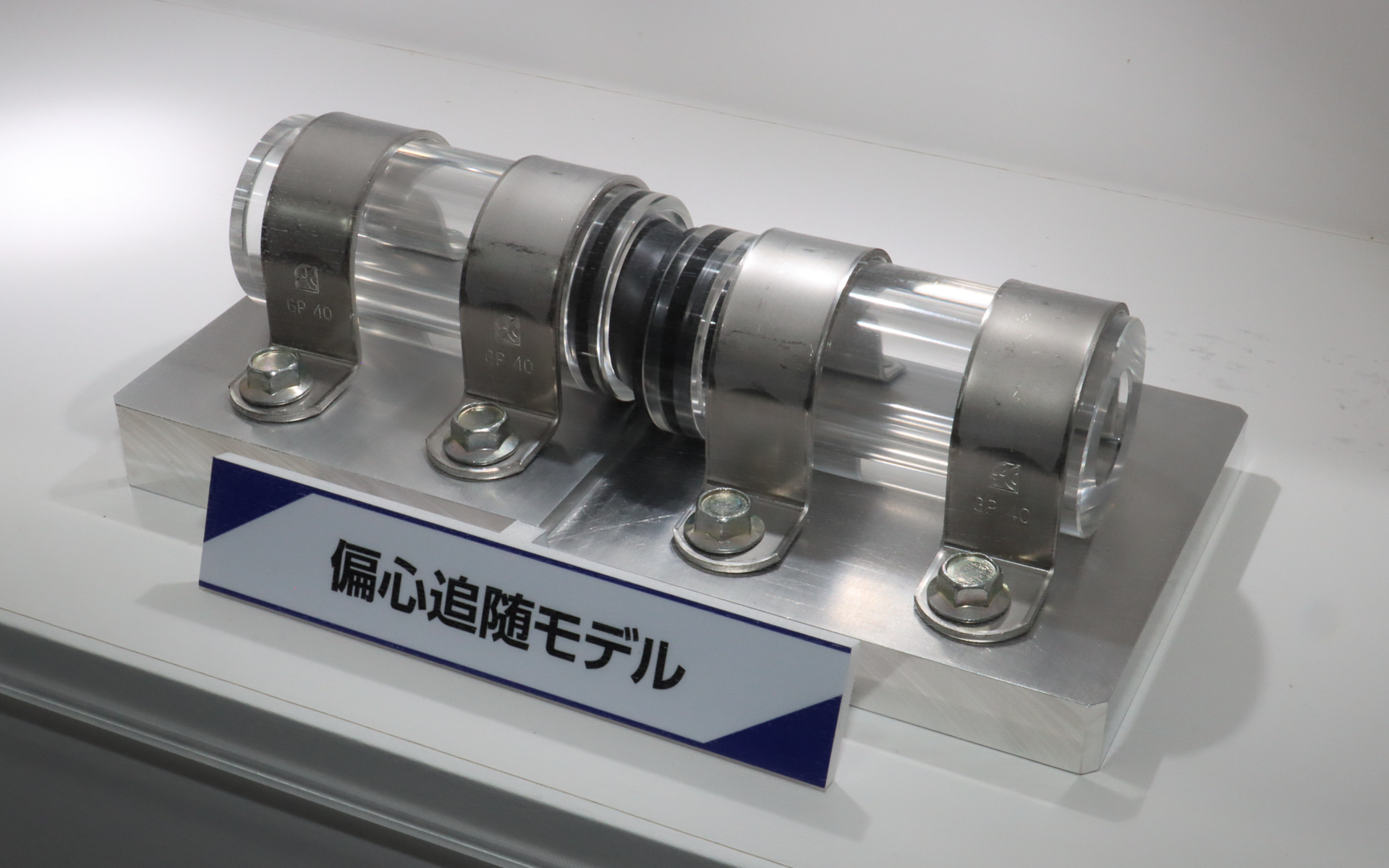 配管用継手シールのデモ展示。高さの異なる2本のパイプの間をつなぐ配管用継手シールは大きく斜めに変形しているが、ゴム嵌合部は歪むことなくパイプに密着している