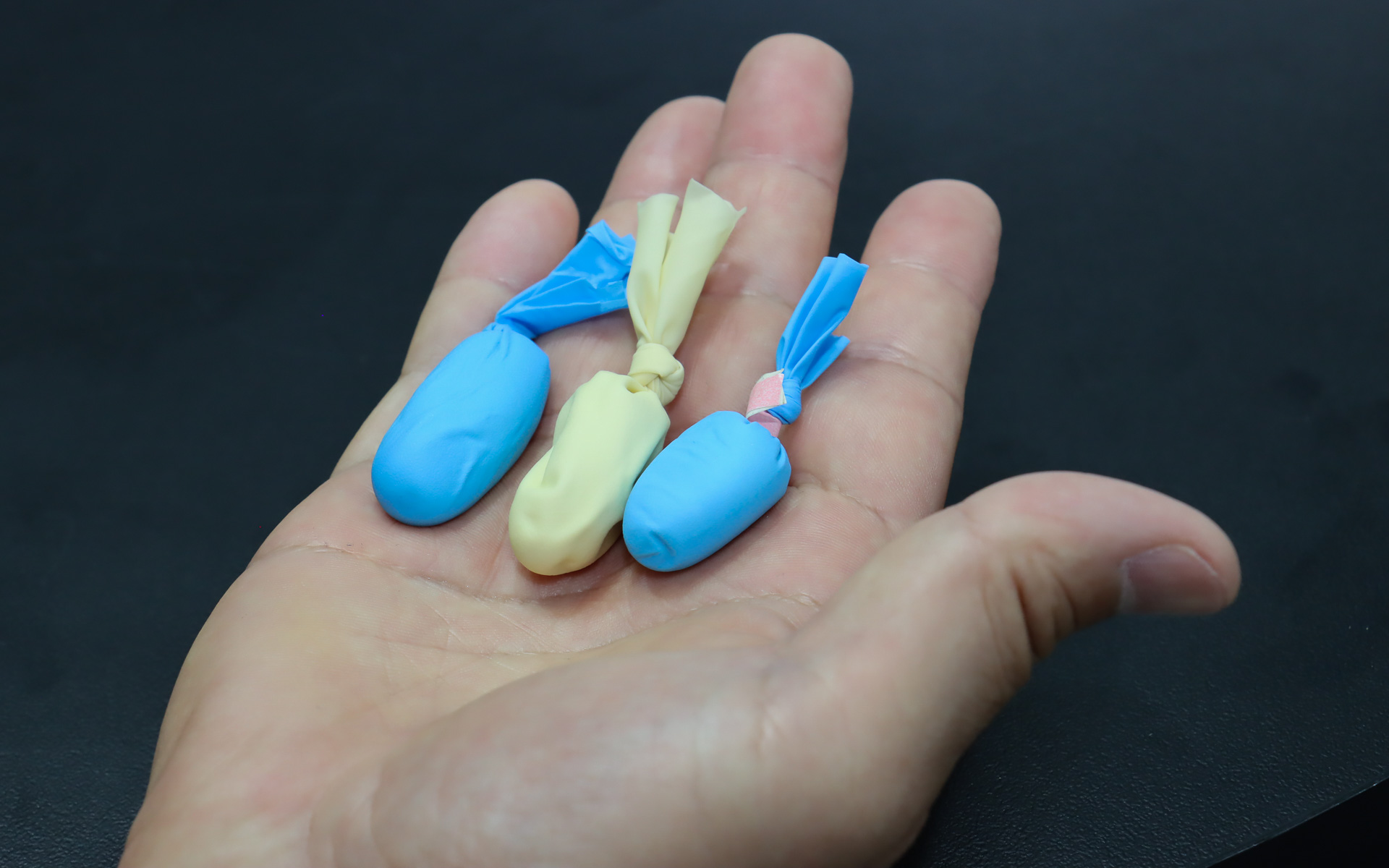 低粘度化によって射出機でも使用可能にしたディスペンサー仕様も開発。会場では標準仕様、ディスペンサー仕様、高熱伝導仕様の3つを袋詰めにして、粘度の違いを指先で感じてもらえるようにしたデモ用素材も用意されていた