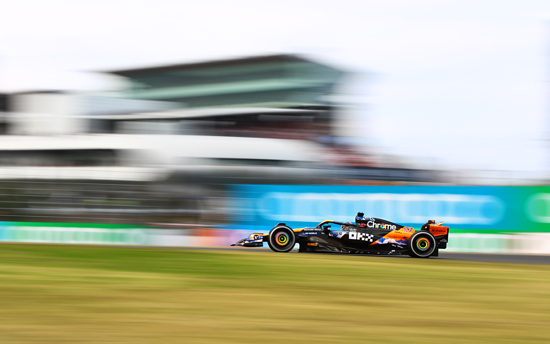 S字に進入するマシンをグランドスタンドとピットビルを背景に入れて、シャッター速度1/40秒で流し撮り