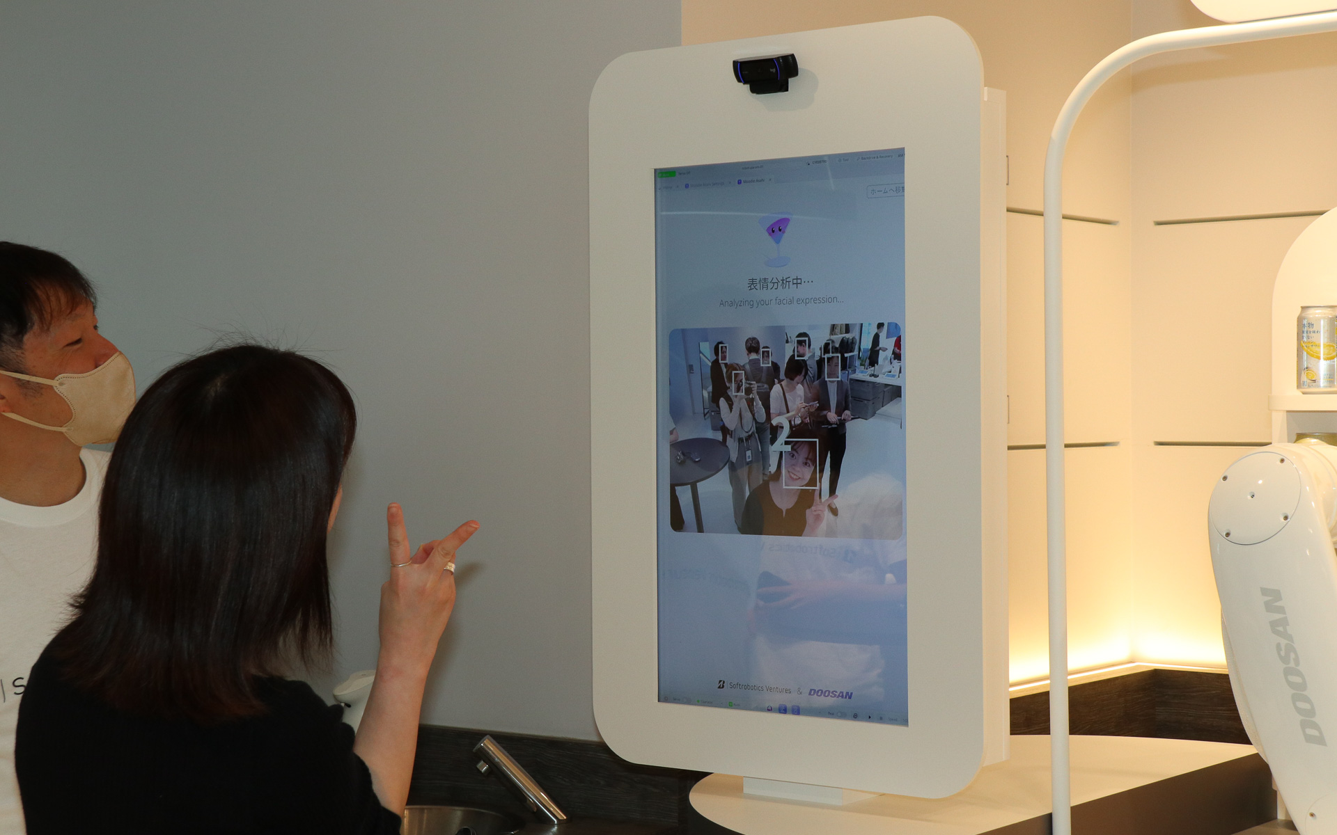 乾杯体験では最初に、左側に設置された大型タッチディスプレイ上のカメラで体験する人の表情を認識