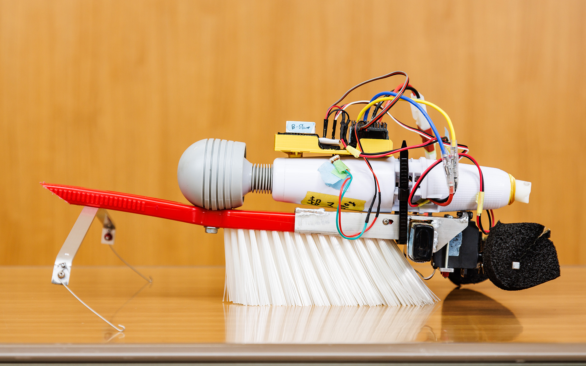 1.5号機をさまざまな角度から。電動マッサージ器の振動をブラシに伝え、ブラシのたわみを推進力にして前進。後方についているストックを動かして方向を変えるのだが、撮影時はストックが左にかたむいてしまっていた。制作費の総額は2万5532円