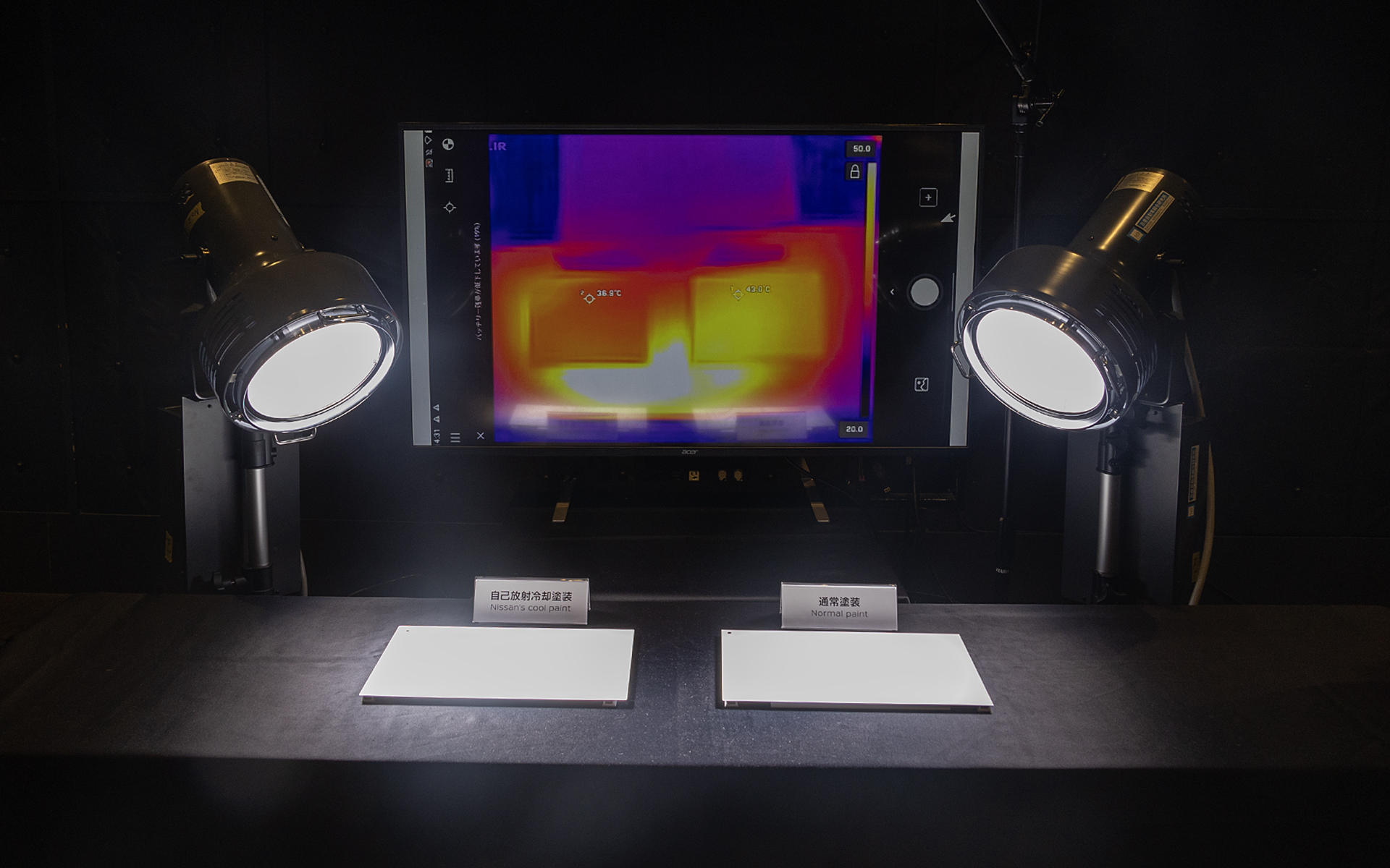 屋内展示もあった。熱の出るライトでそれぞれの塗装を塗ったサンプル板を照射。自己放射冷却塗装（左）は36.5℃、通常塗装（右）は43.8℃
