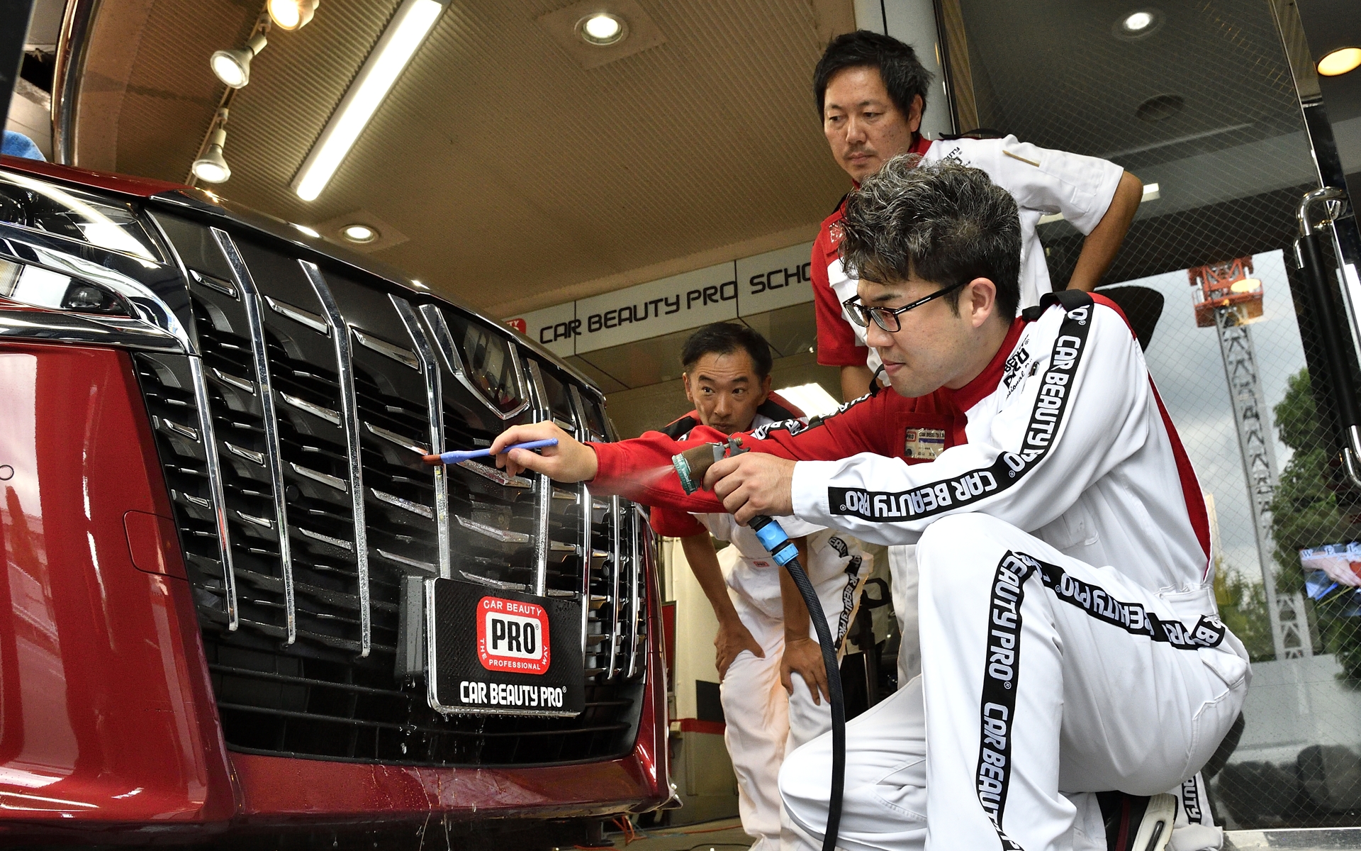 フロントグリル部分を洗浄中。講師はカービューティープロの森山友寛氏で、受講生の真剣な表情が見られる。一見、普通に洗っているようにも見えるが、クルマが傷つかないよう細かい所作まで考え抜かれた動きをしている