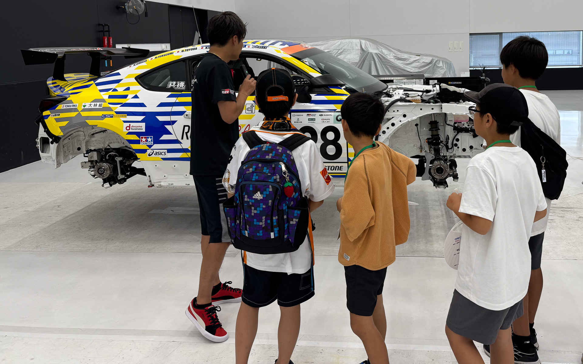 ルーキーレーシングのガレージを子供たち向けに案内する大嶋和也選手