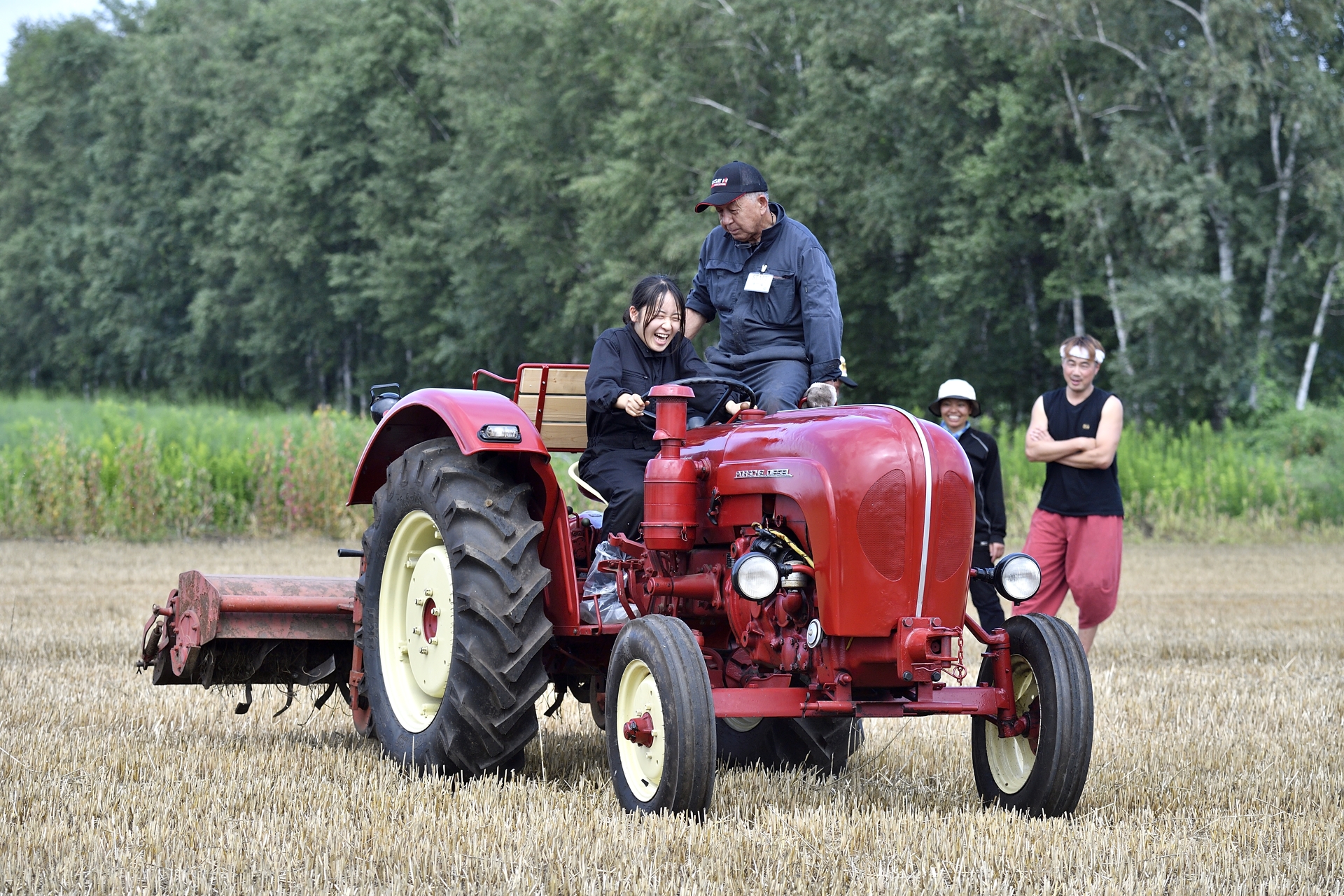 小麦畑でポルシェトラクターに乗る学生たちからは思わず笑みが。自らの手で直したトラクターに乗る気持ちが素直に表れた瞬間だ