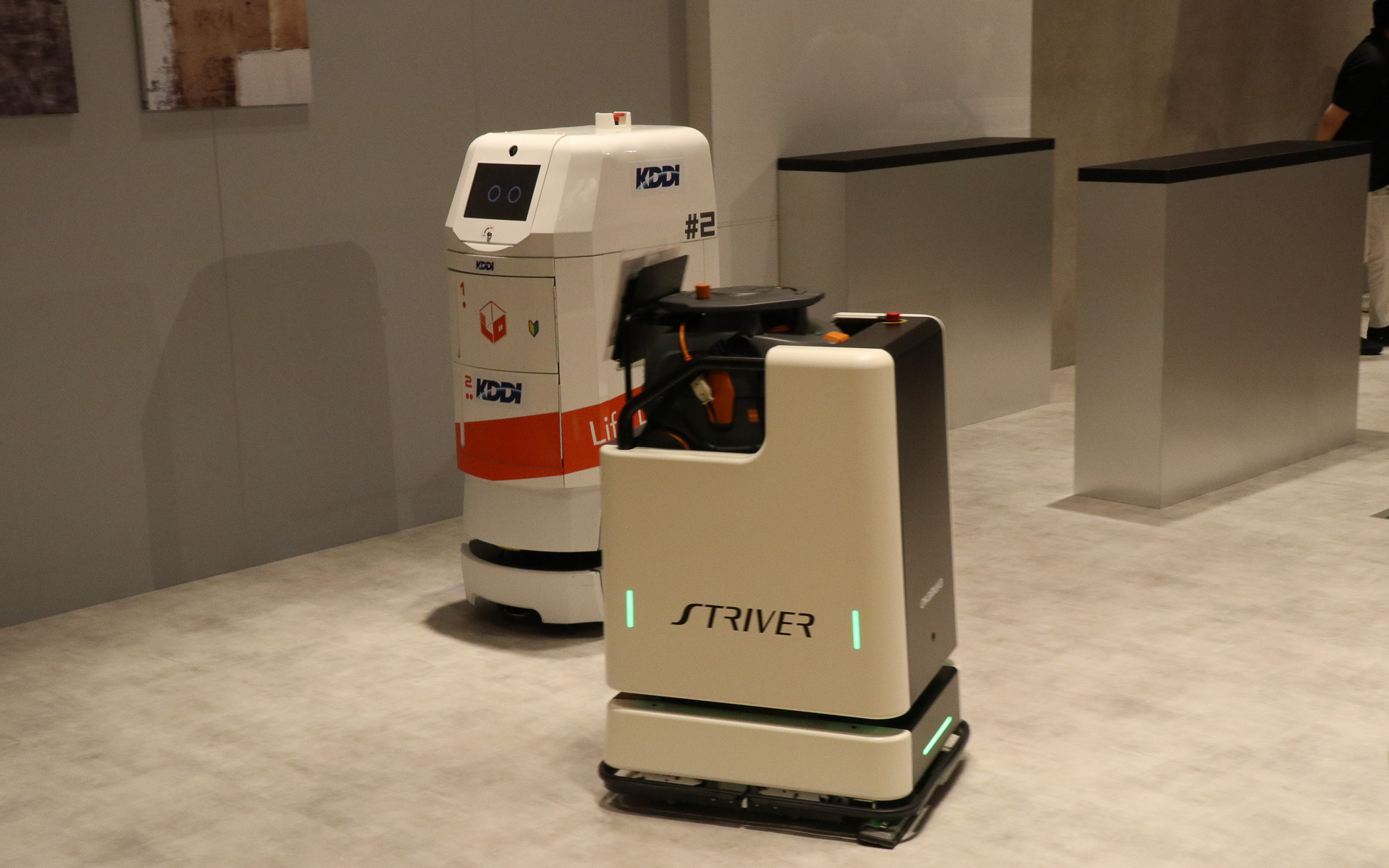 異なるメーカー製のロボットをクラウド管理で協調させるデモ。フロアを掃除する背が低いほうのロボットは常に動き続けているところに、奥で待機している配膳ロボットに飲料水のペットボトルを届けるよう指示を出す。この状況をクラウドに置かれたKDDIの「ロボットプラットフォーム」が管理して、2台のロボットが互いにじゃまをしないようなルートを定めて指示を送り、配膳ロボットはスムーズに手元までペットボトルを届けてくれた